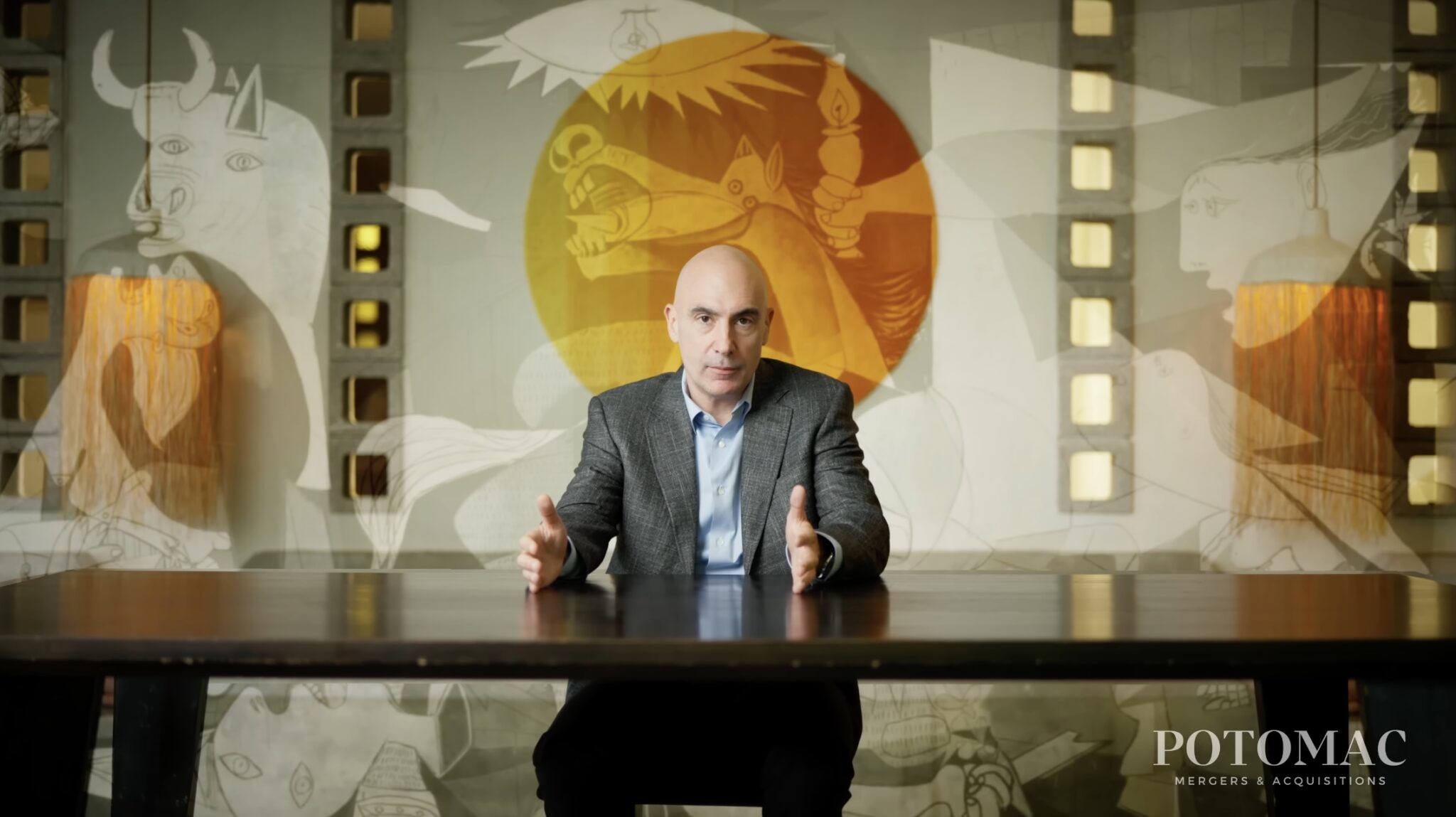A man in a suit sits at a table, gesturing with his hands. Behind him is a mural with abstract animal and human figures. The Potomac Mergers & Acquisitions logo is in the bottom right corner.