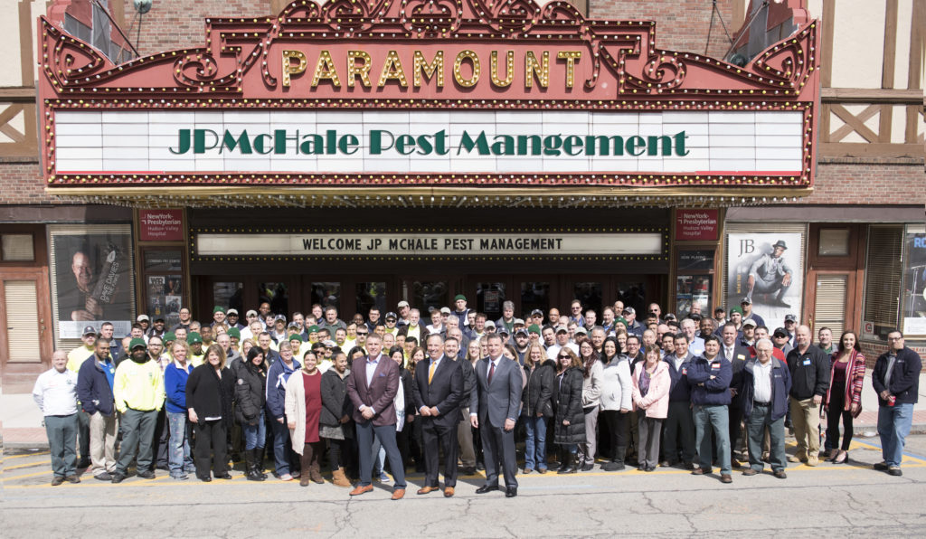 A large group of people stands in front of the Paramount Theatre, under a marquee that reads "JP McHale Pest Management." The group appears to be employees posing for a company photo.